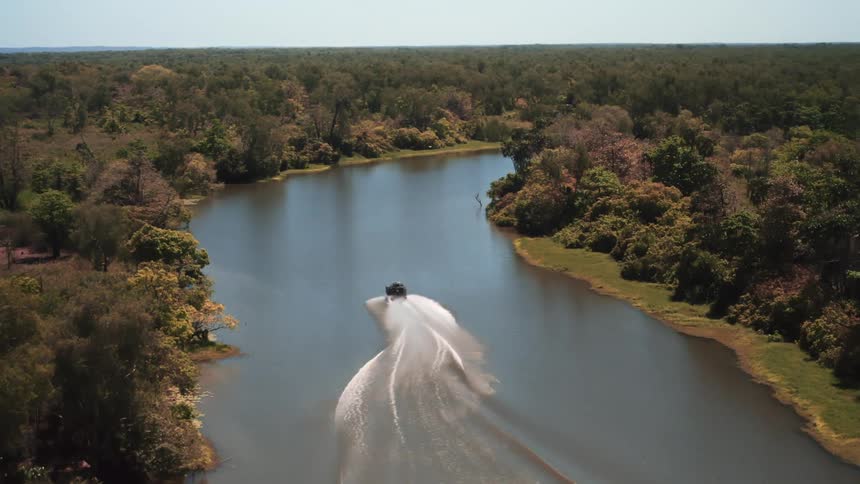 Aerial view of boat traveling along river through forest