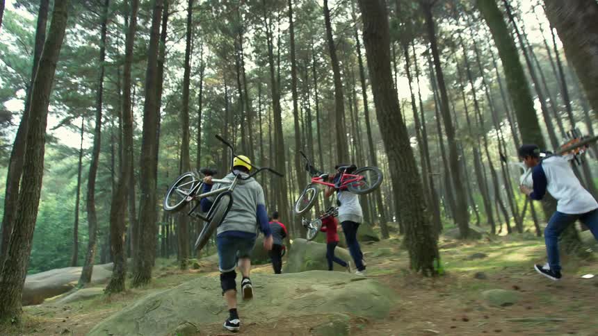 Group of friends running in the forest carrying bicycles at morning