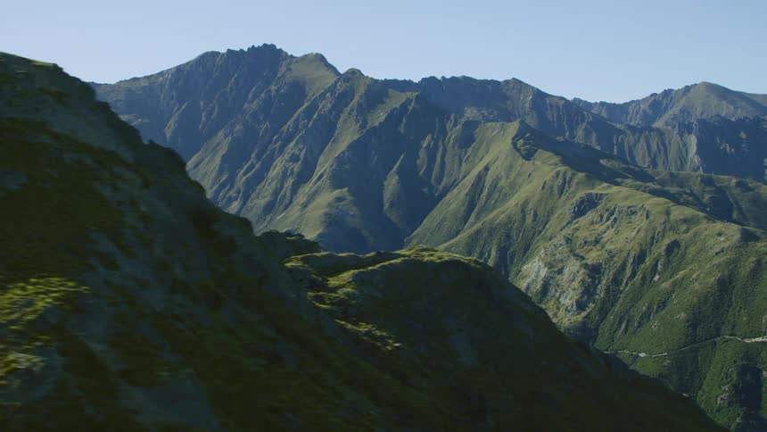 Vegetation covered mountain is separated by steep valley from other mountains covered by mist