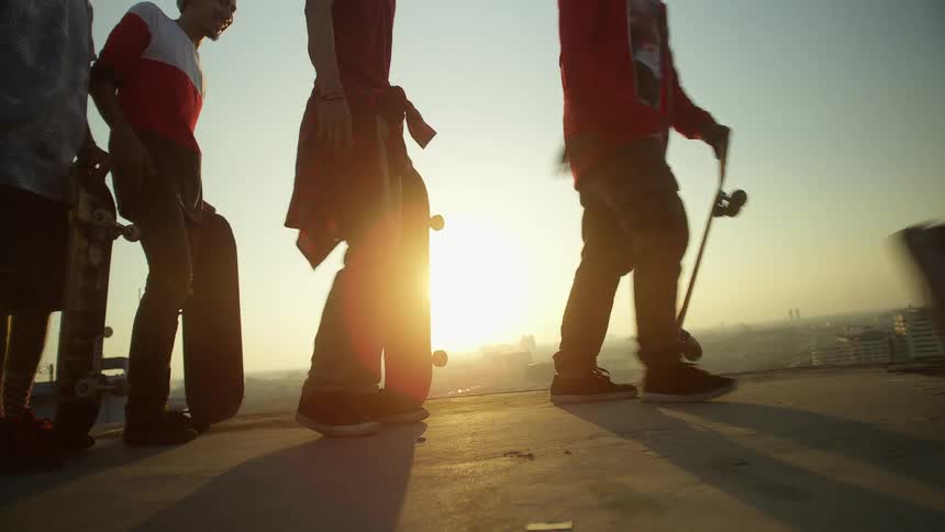 A group of skateboarders in a line drop their boards and skate across a bridge
