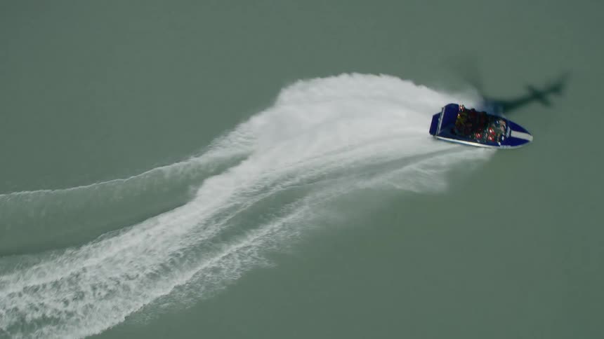 People in a speed boat raise their arms and wave at the helicopter above as they race through the water