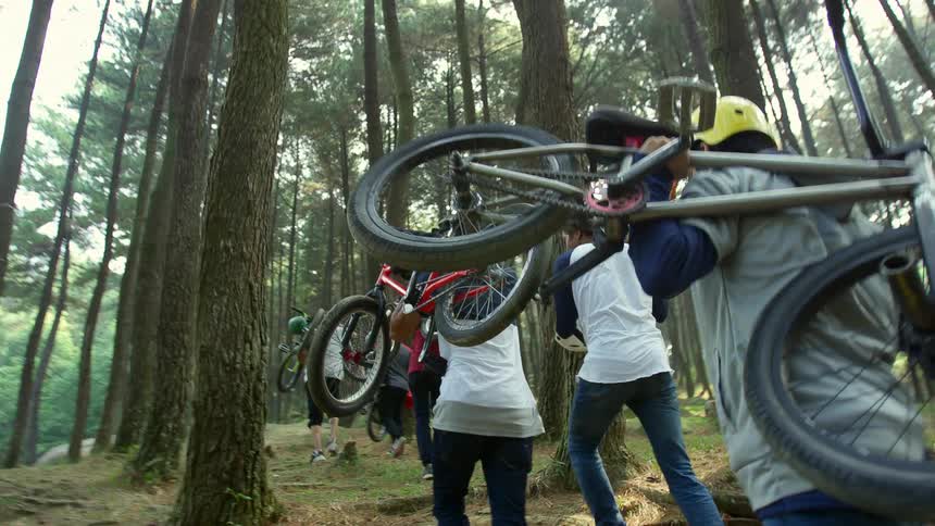 A group of people are carrying mountain bikes up a hill in a forest