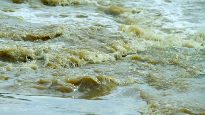 River water flows and churns creating muddy water and foam
