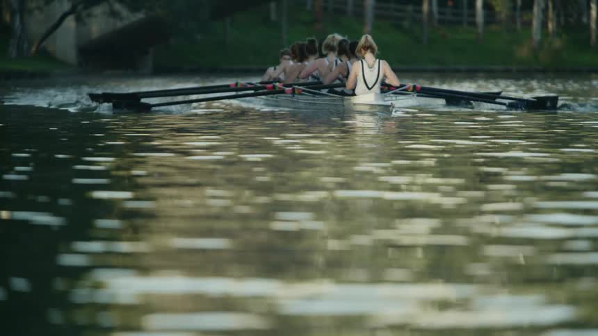 A female rowing crew rows a boat across a lake during the day