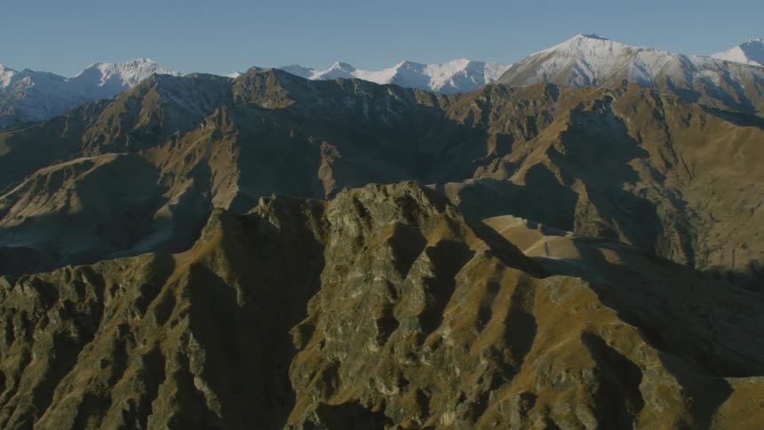 Steep mountains full of shadowy crevices stretch to snow covered mountain on horizon