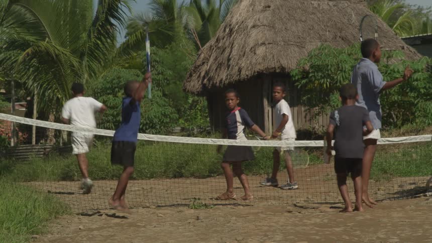 A group of boys play tennis on a lowered net near a hut in a developing country