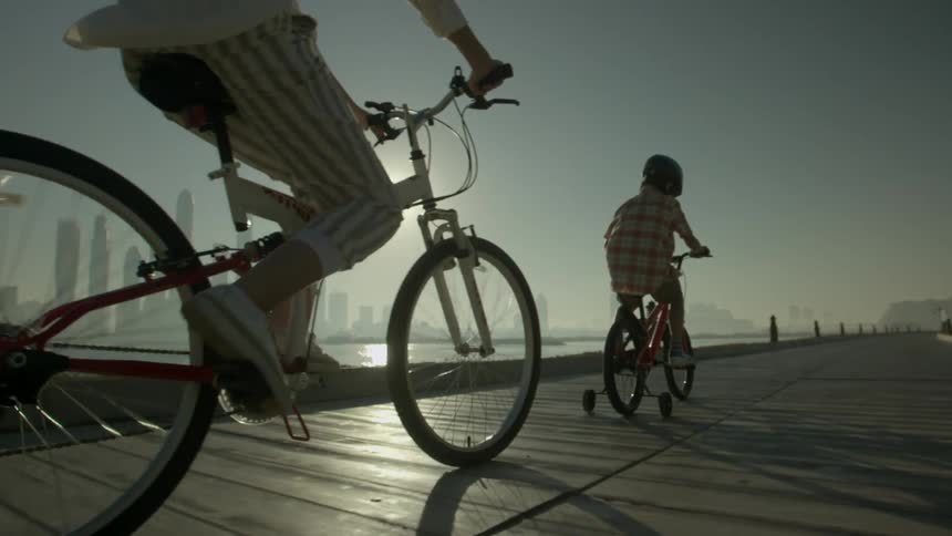 Mother and son riding bicycle on a road near the ocean in front of the city skyline at sunset