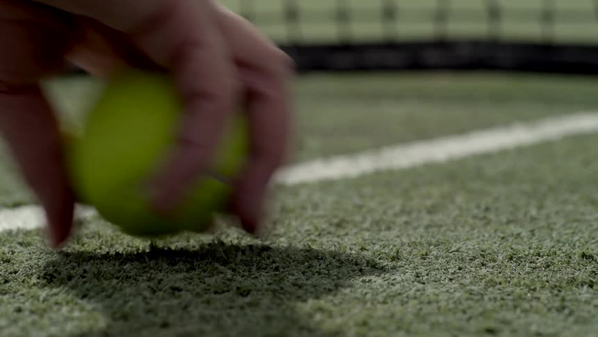 A person picking up a tennis ball in a tennis court with a net in the background