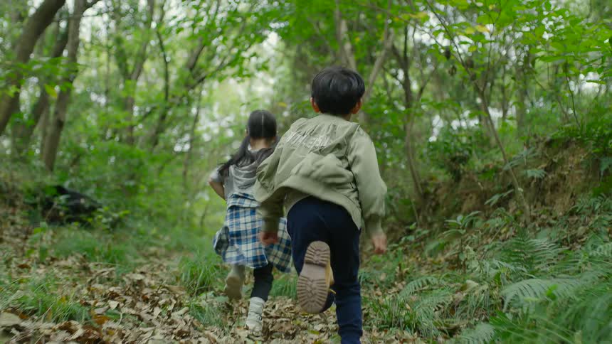 A boy and a girl running in a pathway in a forest with trees the sky and clouds in the background