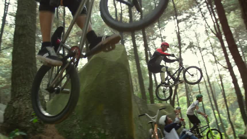 Group of young friends riding bicycles over the big rocks on the forest
