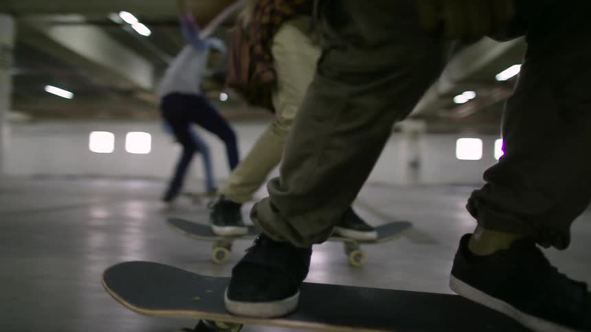A group of teenagers skateboard in sync together in a parking garage