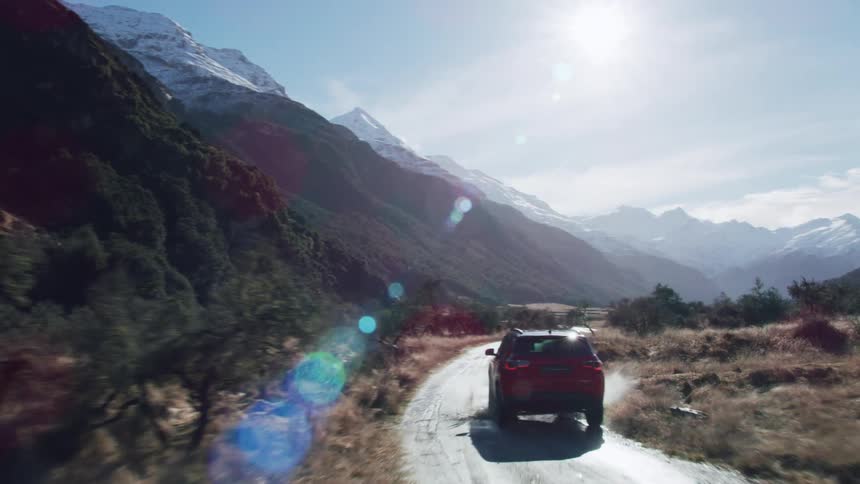 A vehicle drives along a dirt road beside a large mountain