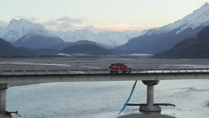 A vehicle driving on a bridge with a mountain range the sky and clouds in the background