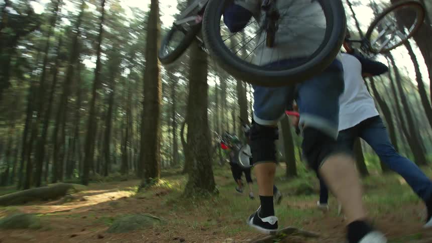 A group of bikers runs through forest carrying bicycles on their shoulders