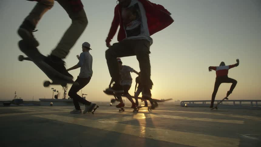 Group of teenagers jumping on skateboards on a park close to the city at sunset