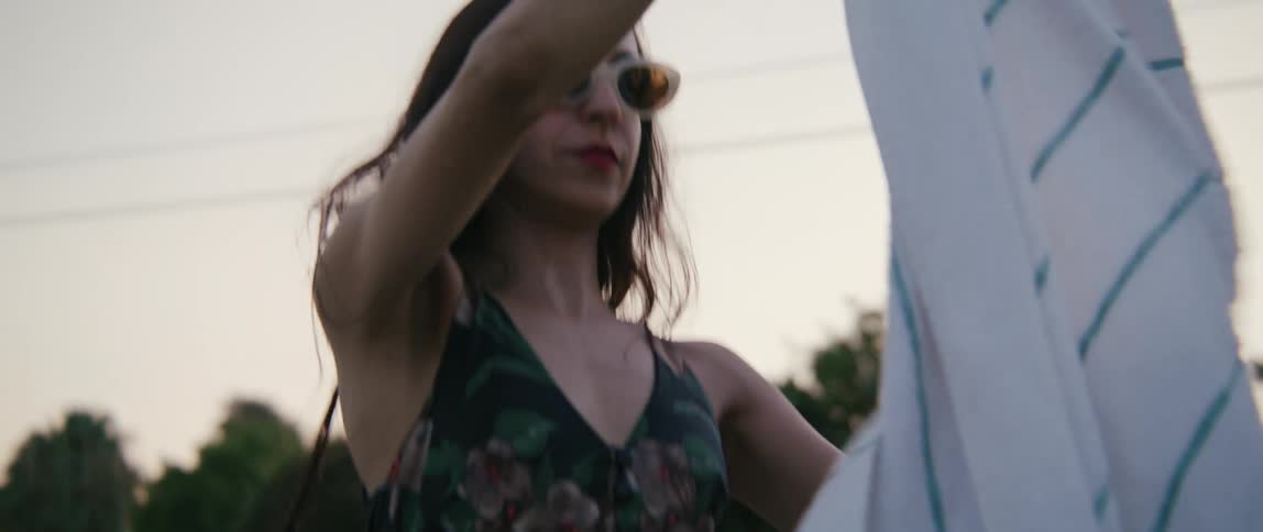 A woman bends down to pick up a beach towel from the ground and wraps it around herself