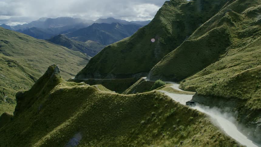 A car travels on a winding mountain road with mountains in the distance