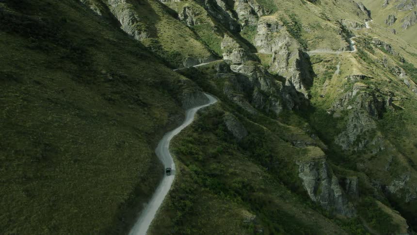 An aerial view of a car driving on a road in a mountain range