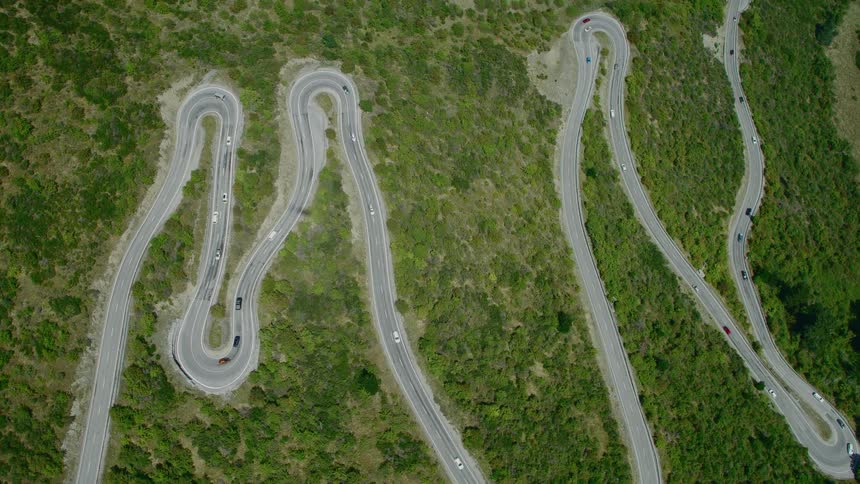 An aerial view of cars driving on a twisty road through a grassland area