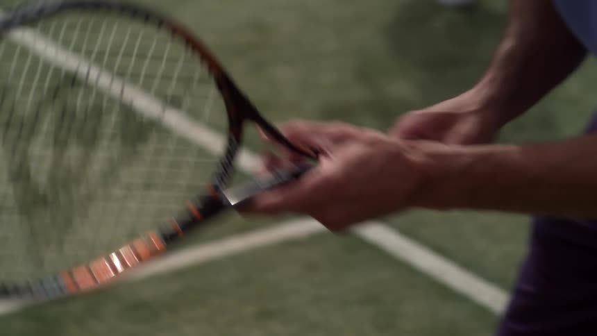 Tennis player rotates racket in his hands waiting in corner of tennis court