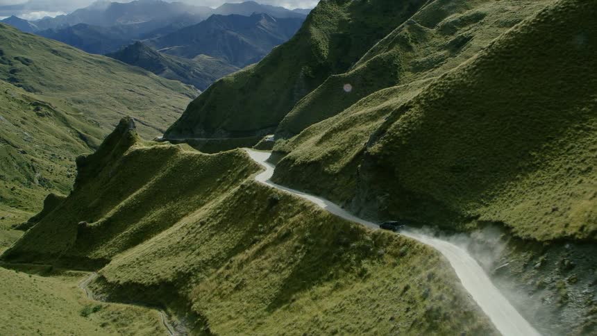 A vehicle drives on the road on the side of the mountain