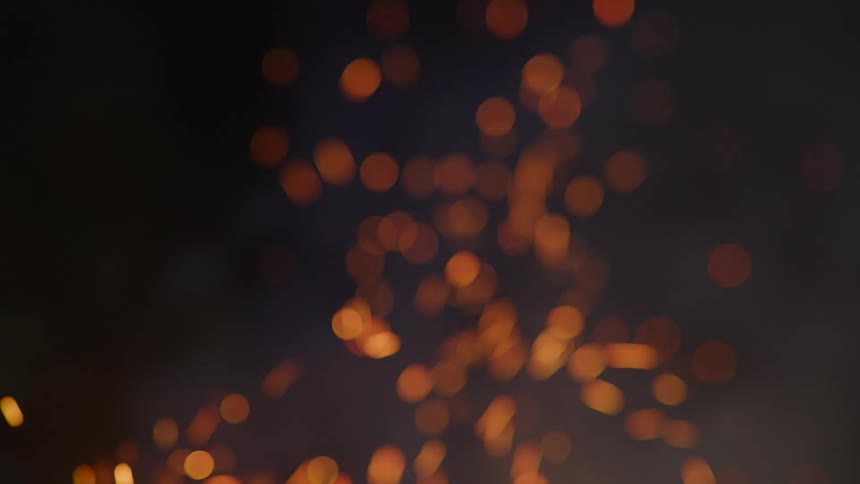 Sparks rise from burning wood of bonfire glowing orange against black of night