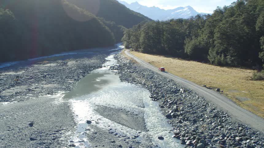 A vehicle driving on a road next to trees with a mountain range the sky and clouds in the background