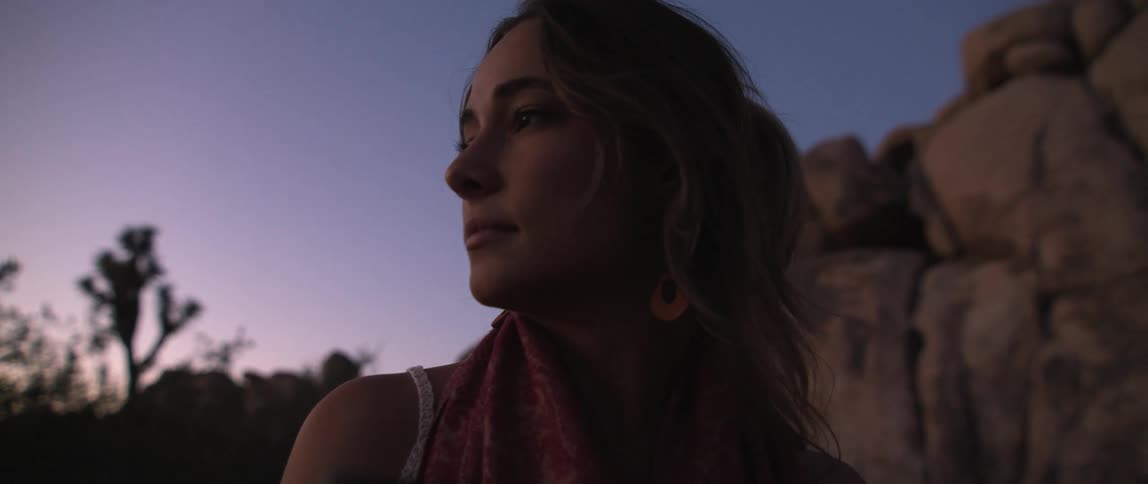 Close up of a young woman standing next to a rock wall on the desert at sunset
