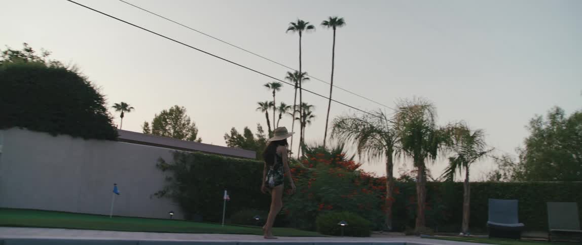 A woman is walking by an outdoors pool at dusk