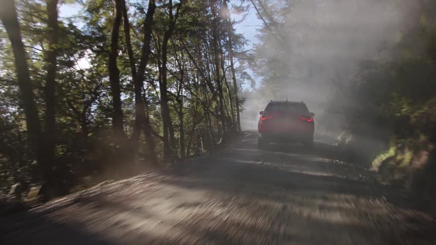 A vehicle driving on a dirt road surrounded by trees with the sky and clouds in the background