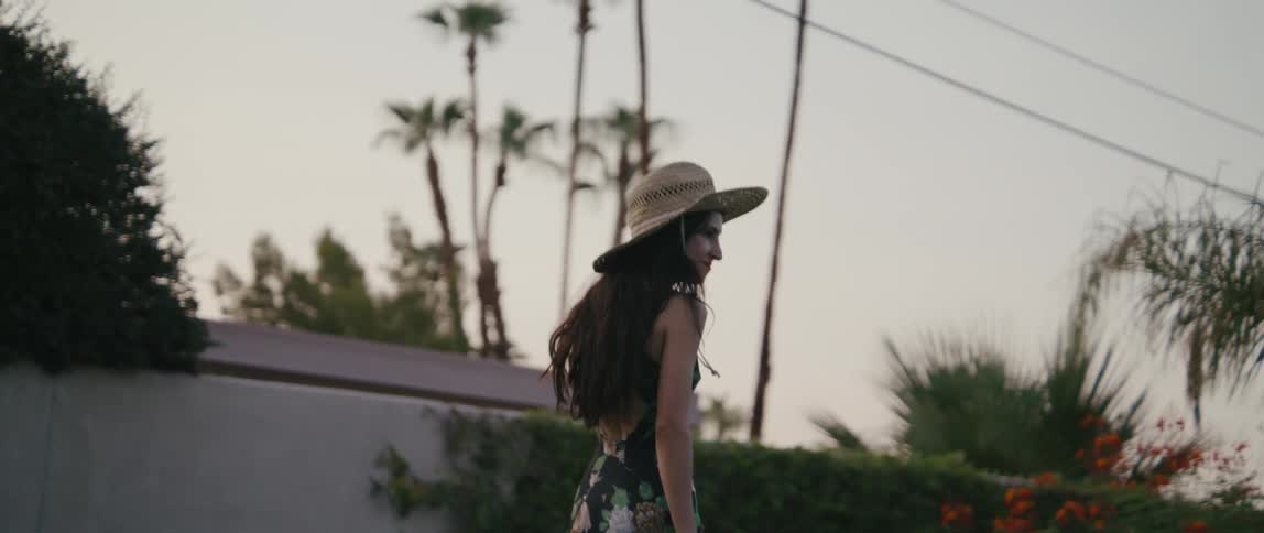 A woman wearing a hat is walking down a neighborhood street