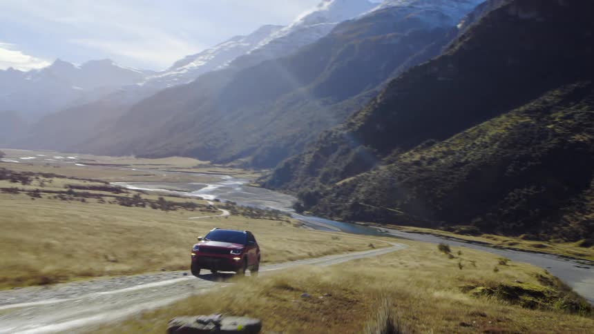 Aerial view of a car driving on a dirt road on a narrow valley between mountains at morning