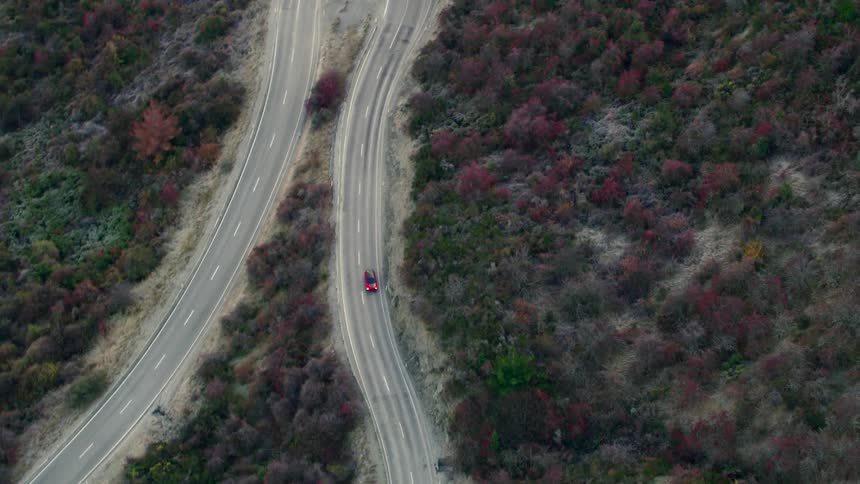 A red car is traveling on a winding road
