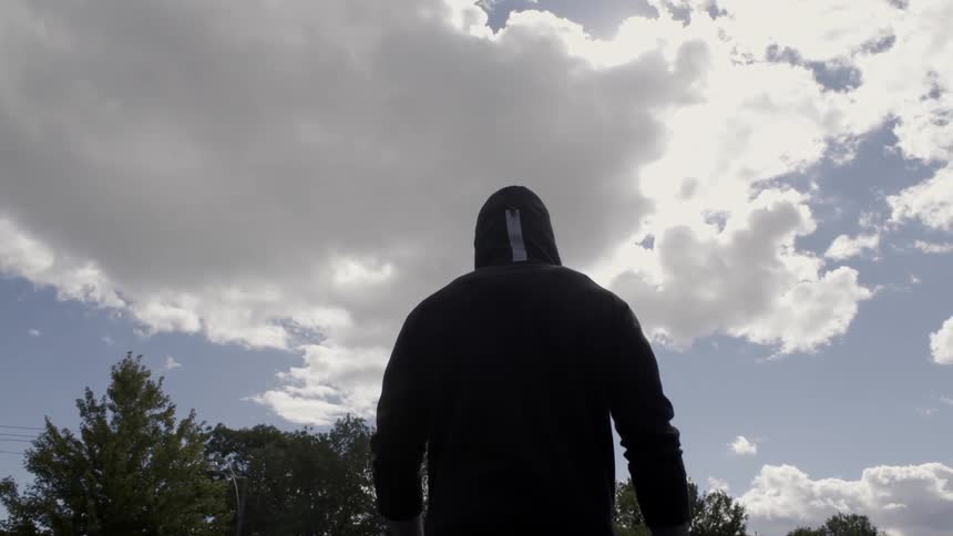 A person in a black hoodie walks on a cloudy day