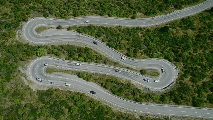 Vehicles drive along winding road surrounded by woods