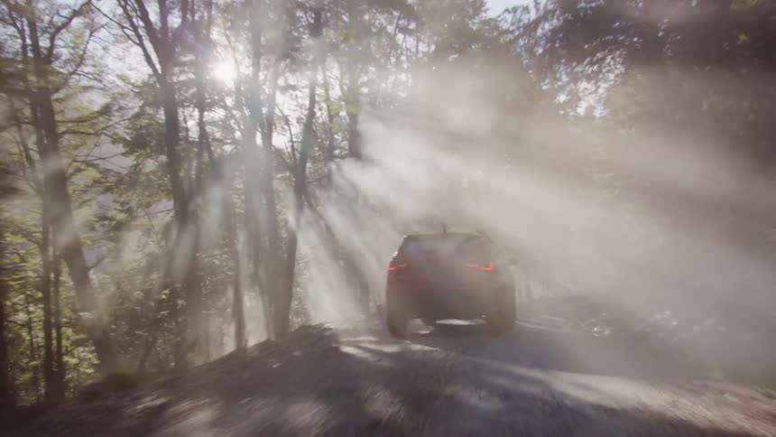 An suv travels on a narrow dirt road as the sunshine beams through the trees