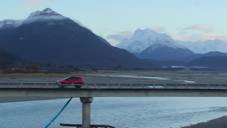 A vehicle travels across a narrow bridge spanning a river in the countryside during the day