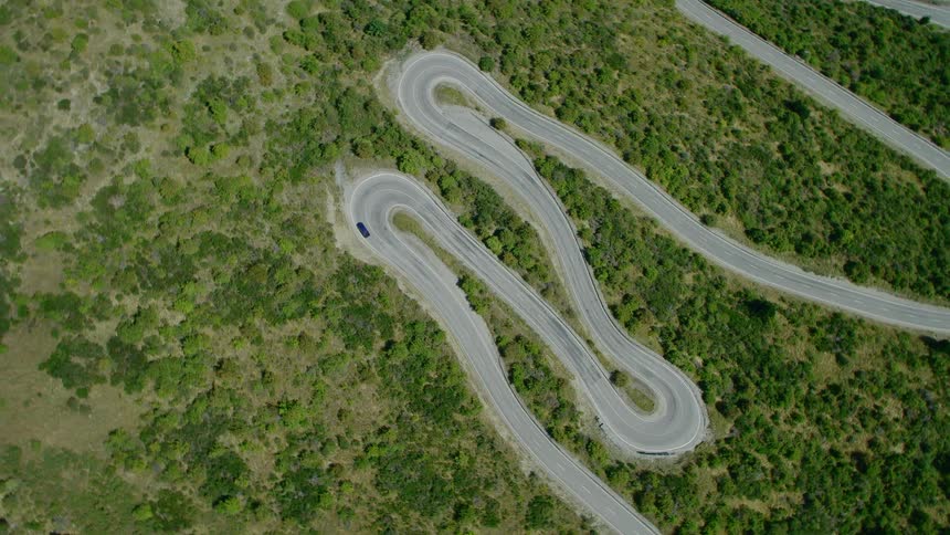 A car is traveling on a winding and remote highway on sunny day