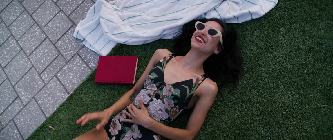 A woman wearing sunglasses is laying on turf and laughing
