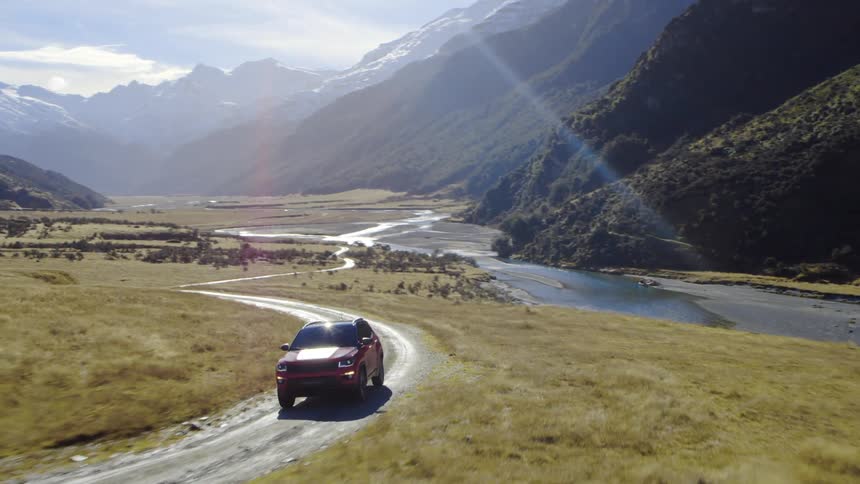 A vehicle is driving on a dirt trail by the mountain