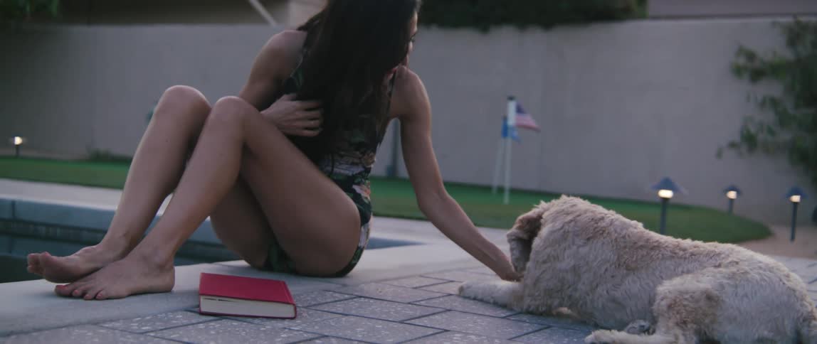 A woman sits beside a pool playing with a dog