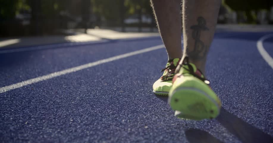 A man wearing brightly colored track shoes walks on an athletic track