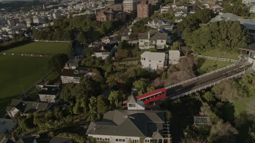 A tram travels down tracks on a bridge on a hill slope past homes built into the hillside