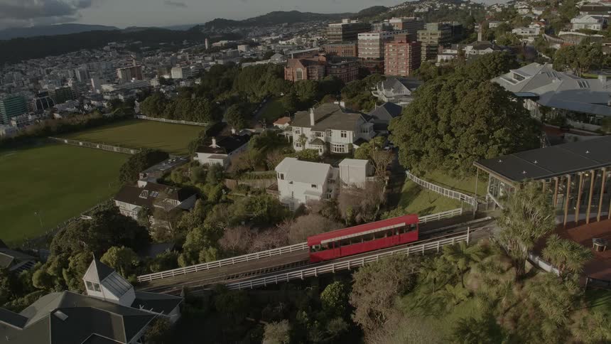 A tram travels up a track toward a station with buildings built into a hill