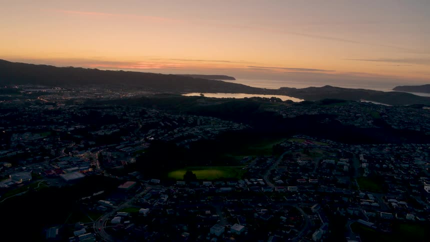 Hills and a lake sit next to a city as vehicles travel on the city streets at night