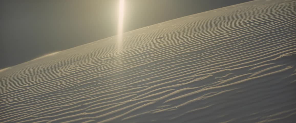Wind blowing over the white sand on a dune in the desert under the sun