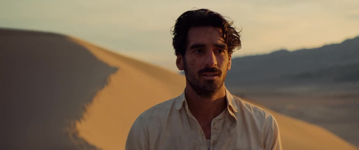 Disheveled looking man turns to look behind him while standing in the desert
