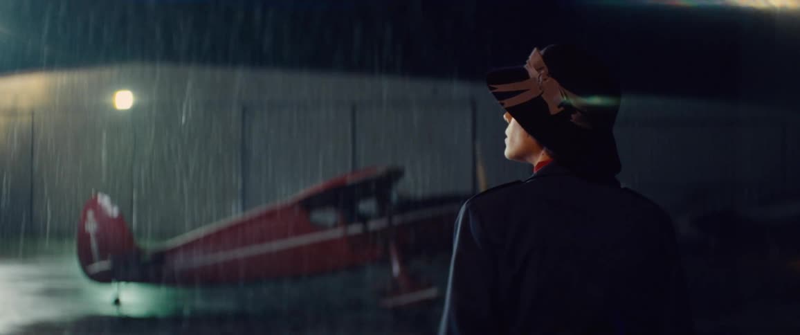 A woman walks toward a red vintage airplane just as it takes off