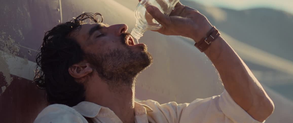 A man drinks from a water bottle while sitting against a plane