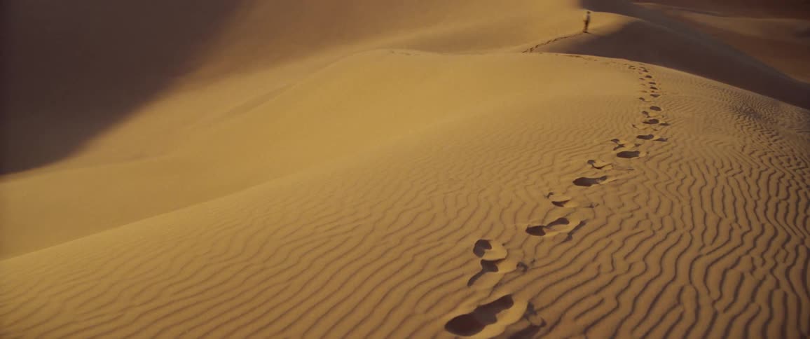 Human footprints run along the top of a vast sand dune in the desert